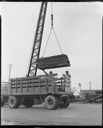 Crane loading or unloading wooden railroad ties from truck